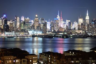 Illuminated buildings by sea against sky at night