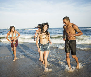 Cheerful couples walking on shore against sky