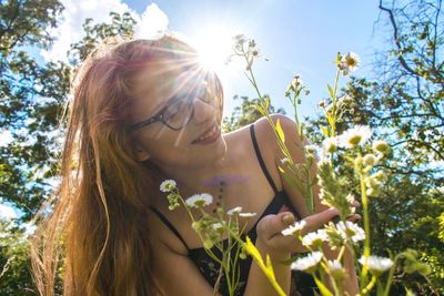 Smiling young woman touching white flowers during sunny day