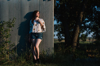 Full length of young woman standing against wall on field