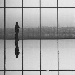 Silhouette man standing on glass against sky