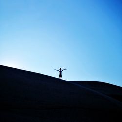 Low angle view of silhouette man standing against clear blue sky