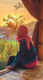 Side view of girl looking away while sitting on plant against sky