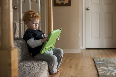 Toddler boy sitting on stairs at home taps on his electronic