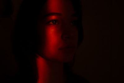 Close-up portrait of young woman against black background