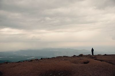 Silhouette man standing on cliff against cloudy sky