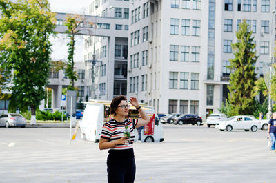 Side view of woman using mobile phone with smoothie in her hands in city against clear sky