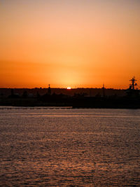 Silhouette city by sea against romantic sky at sunset