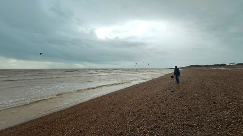 Rear view of man walking at beach against sky