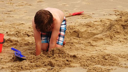 Shirtless boy digging sand at beach