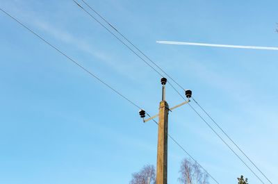 Low angle view of power lines and contrails against a blue sky