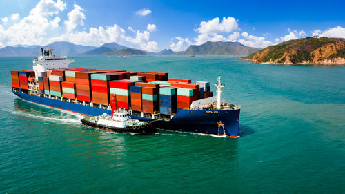 Containers ship and tugboat sailing open sea and mountain background business