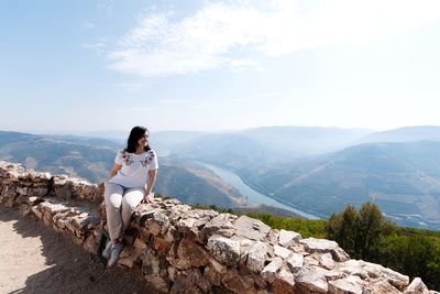 Woman sitting on retaining wall against mountains