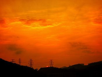 Low angle view of silhouette electricity pylon against dramatic sky