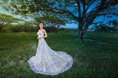 Young woman in gown standing on field against trees