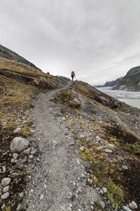 Rear view of man walking on mountain road by river against sky