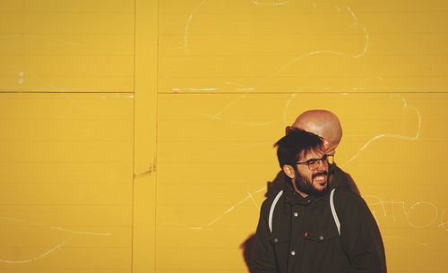 Portrait of young man standing against yellow wall