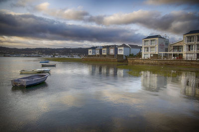 Boats moored on river by buildings in city against sky