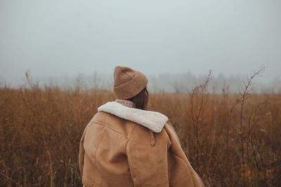 Women standing in a foggy late autumn winter field against sky looking back with negative space