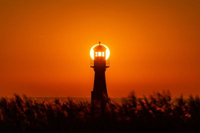 Silhouette lighthouse on field against sky during sunset