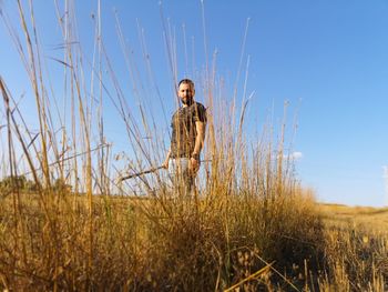 Portrait of young man standing on field against sky