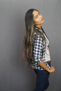 Young woman looking away while standing against wall