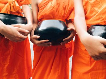 Midsection of monks holding container while standing in shrine