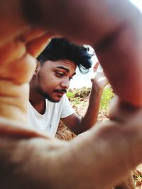 Close-up of man seen through fingers outdoors