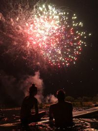 Rear view of people looking at firework display at night