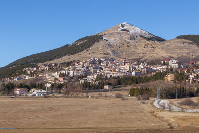 Scenic view of townscape by mountains against clear blue sky