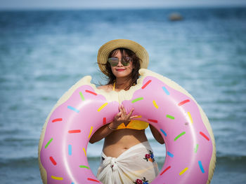 Portrait of woman holding donut pattern inflatable ring at beach