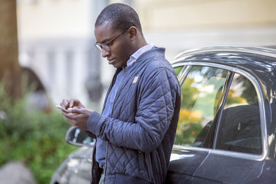 Young man leaning against car using cell phone