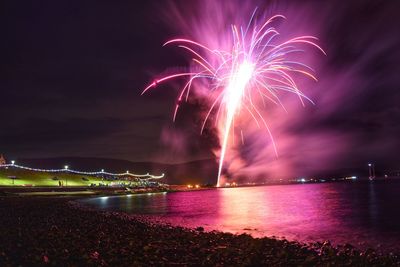 Firework display over sea against sky at night