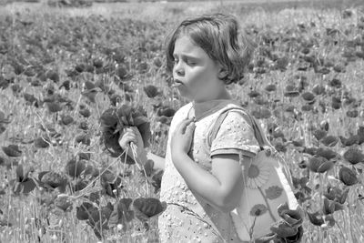 Girl holding poppy flowers while standing amidst plants on field