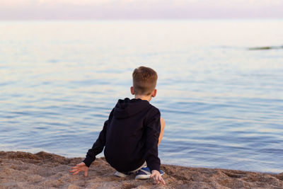 Rear view of boy crouching at beach