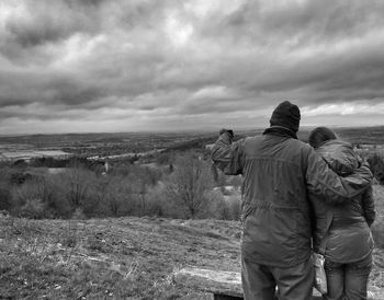 Rear view of man standing on landscape against cloudy sky