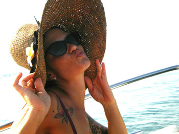 Young woman wearing hat while pouting in cruise ship by sea against sky