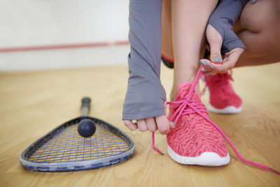 Low section of woman tying shoelace by racket on floor