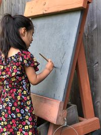 Girl holding paintbrush on blackboard