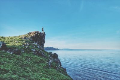 Man standing on cliff by sea against clear blue sky