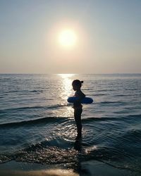 Girl standing in sea against sky during sunset