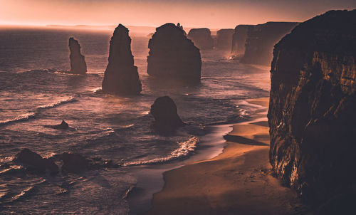 Rock formation on beach against sky during sunset