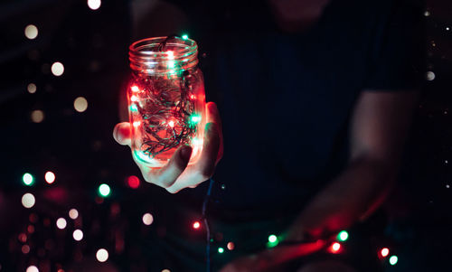 Midsection of man holding illuminated lights in glass jar at night
