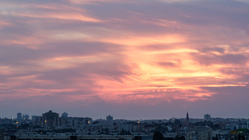 Cityscape against dramatic sky during sunset