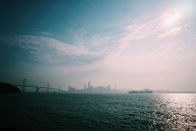 View of city at waterfront against cloudy sky