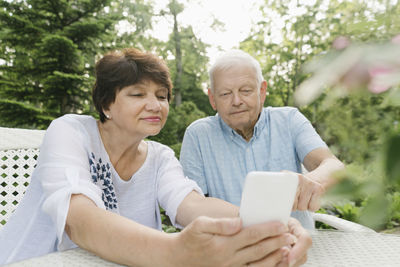 Portrait of senior couple sitting at garden table looking at cell phone