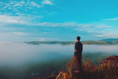 Full length of man looking at mountains while standing against sky during foggy weather