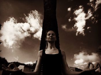 Low angle view of woman meditating in yard against sky