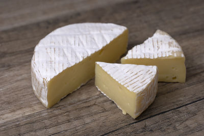 Round brie cheese with a section cut out over wooden background, close up view.