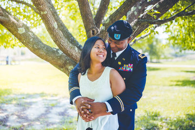 Smiling soldier embracing woman while standing against trees at park
